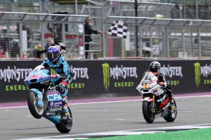 Met een fraaie wheelie komt Jake Dixon als winnaar over de finish voor Aron Canet.
